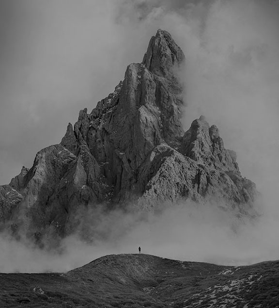 A man standing at the bottom of a mountain surrounded with fog